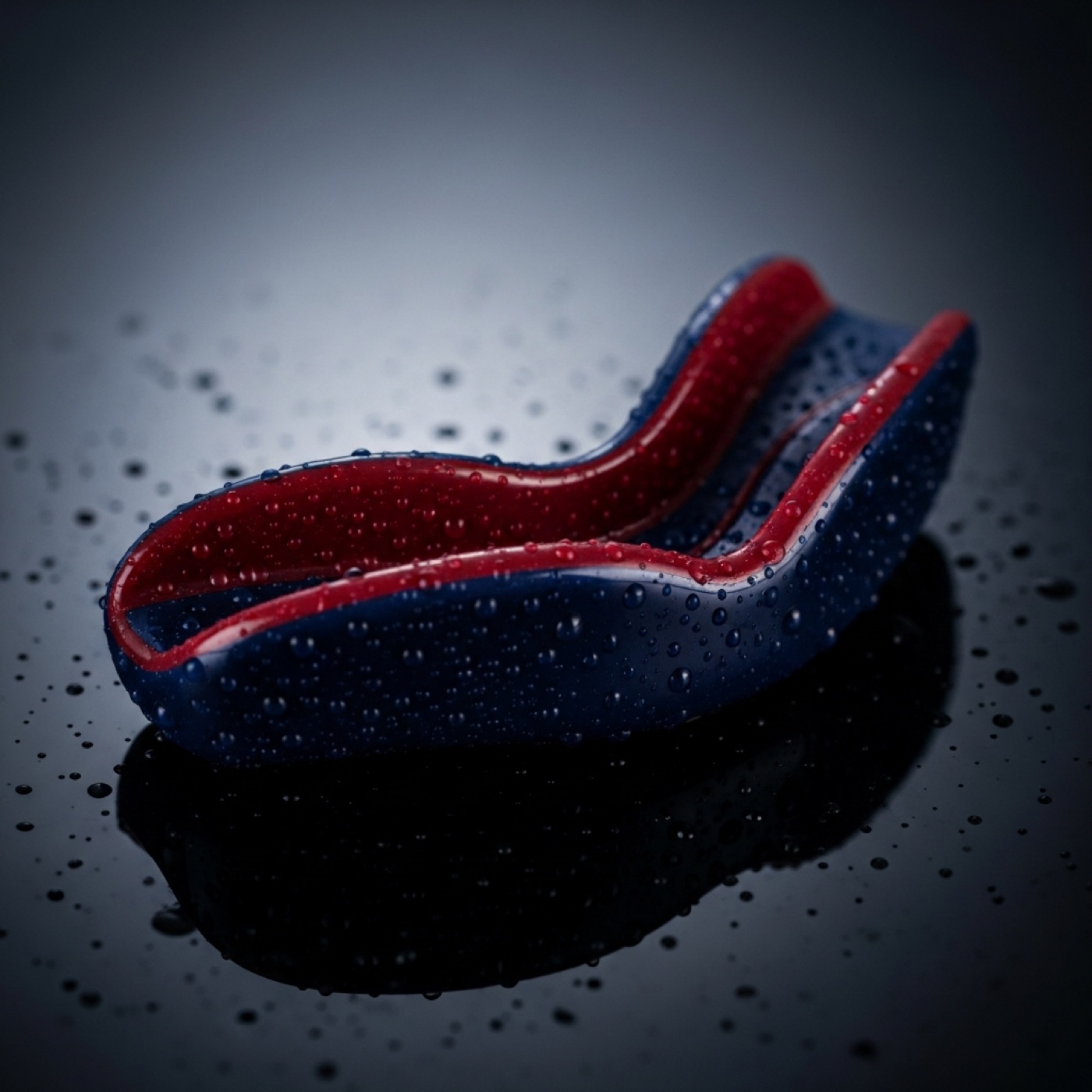 Macro close-up of a glossy navy and claret mouthguard with water droplets